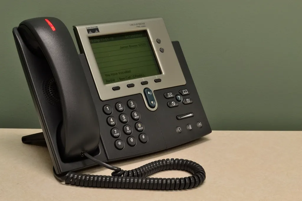 A desk IP phone with its handset and coiled cord on an office desk